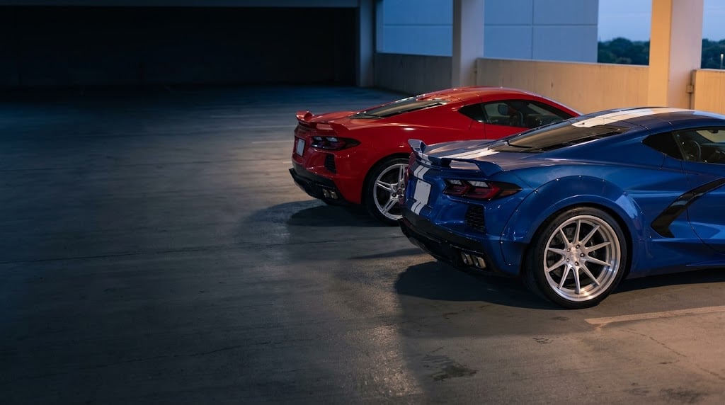 2027 Corvette Grand Sport wide body next to a narrow-body C8 Stingray, rear three-quarter view